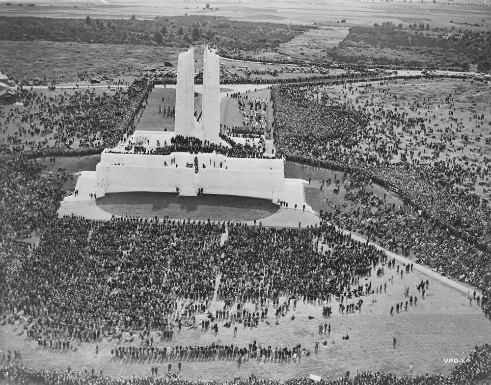 Photographie en noir et blanc – Vue aérienne du monument et de la foule qui l’entoure. L’emblématique sculpture Mère Canada est couverte d’une toile foncée.